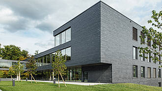 Auf dem Bild ist ein Gebäude mit dunkelgrauen Schieferschindeln an der Fassade zu sehen. 