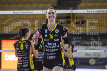 Auf dem Foto sieht man Lara Berger, die übers ganze Gesicht strahlt, in Sportkleidung vor einem Volleyball-Netz während eines Spiels. Die junge Frau war früher Profi-Volleyballerin und studiert inzwischen Gesundheitsmanagement an der Hochschule Aalen.