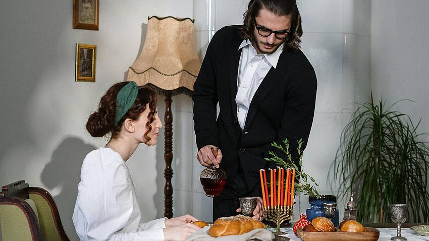 Ein junges jüdisches Paar sitzt an einem gedeckten Esstisch, auf dem ein Chanukka-Leuchter steht. dem ein 