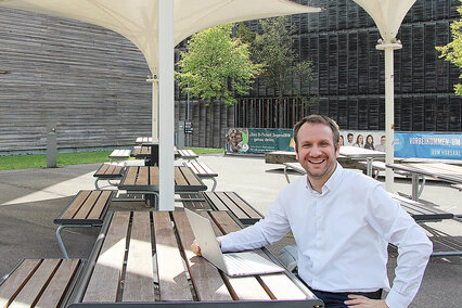 Prof. Dr. Daniel Gartner sitzt mit seinem Laptop unter den Sonnenschirmen auf dem Campus Burren.