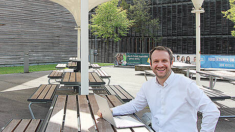 Prof. Dr. Daniel Gartner sitzt mit seinem Laptop unter den Sonnenschirmen auf dem Campus Burren.