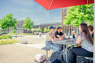 Vier Studierende sitzen an einem Tisch, im Außenbereich der Cafeteria am Burren.