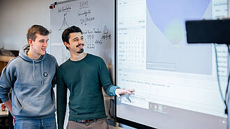 Zwei Studierende des Masterstudiengangs Elektrotechnik unterhalten sich vor einem Whiteboard