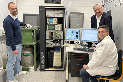 Der Chemie-Student Alexander Ehrlinspiel steht neben dem Gammaspektrometer im Isotopenlabor der Hochschule Aalen und hält eine Probe mit Gartenerde in der Hand. Daneben sind Laborleiter Dr. Wolfgang Schulz und Mitarbeiter Silvin Hippich zu sehen.