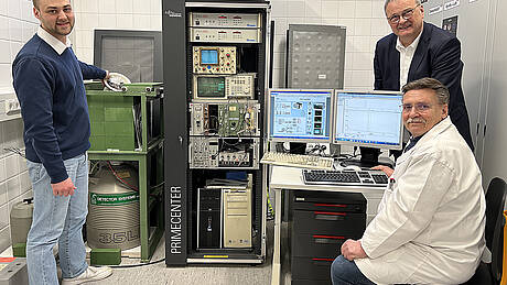 Der Chemie-Student Alexander Ehrlinspiel steht neben dem Gammaspektrometer im Isotopenlabor der Hochschule Aalen und hält eine Probe mit Gartenerde in der Hand. Daneben sind Laborleiter Dr. Wolfgang Schulz und Mitarbeiter Silvin Hippich zu sehen.