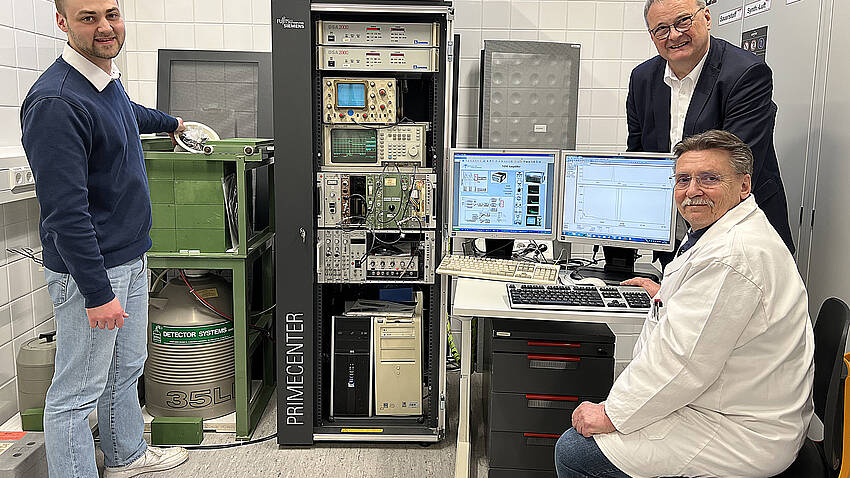 Der Chemie-Student Alexander Ehrlinspiel steht neben dem Gammaspektrometer im Isotopenlabor der Hochschule Aalen und hält eine Probe mit Gartenerde in der Hand. Daneben sind Laborleiter Dr. Wolfgang Schulz und Mitarbeiter Silvin Hippich zu sehen.