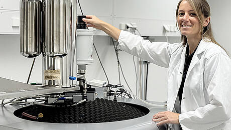 Kathrin Geiger, eine junge Frau mit langen, dunkelblonden Haaren und gekleidet in einem weißen Kittel, steht im Institut für Materialforschung der Hochschule Aalen an einem Vibrationsmagnetometer. Die Masterandin untersucht Kathrin Geiger die magnetischen Eigenschaften ihrer Materialproben. Die Masterandin forscht am Institut für Materialforschung Aalen (IMFAA) der Hochschule Aalen an neuen Magnetwerkstoffe mit weniger kritischen Rohstoffen.