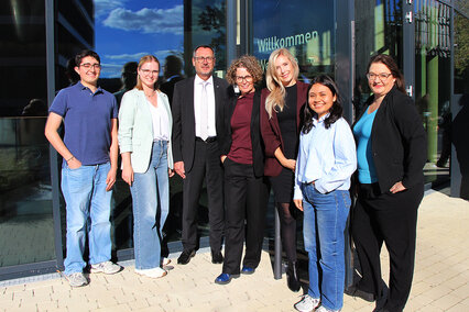 Ostwürttemberg wird „Leuchtturm-Region MINTernational“ Vor dem Digital Innovation Space (DIS) stehen Adrian Rojas, Lorena Lenz (Studiengangskoordinatorin), Thilo Rentschler (Hauptgeschäftsführer der IHK Ostwürttemberg), Prof. Dr. Anja Dieckmann (Prorektorin für Internationales), Sarah Dotschkal (MINT-Referentin Region Ostwürttemberg) Sharon Vásquez und Prof. Dr. Doris Aschenbrenner. Die Gruppe freut sich über die Auszeichnung Ostwürttembergs als „Leuchtturm-Region MINTernational“ und strahlt in die Kamera. Hinter ihr ist an der Tür die Aufschrift "Willkommen" zu sehen.