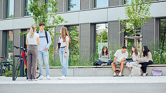 Gruppen von Studierenden stehen am Außenbereich des WIN-Gebäudes und unterhalten sich.