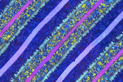 Auf dem Foto sieht man das Gefüge eines Metalls. Die die farbenfrohe Wunderwelt der mikroskopischen Strukturen wurden durch ein Hochleistungsmikroskop sichtbar gemacht. Die geometrische Anordnung in blauen, violetten und grünlichen Streifen sieht fast wie ein Kunstwerk aus.