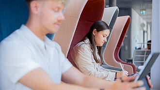 Zwei Studierende sitzen an Einzeltischen in der Bibliothek und lernen. Zwei Studierende sitzen an Einzeltischen in der Bibliothek und lernen.