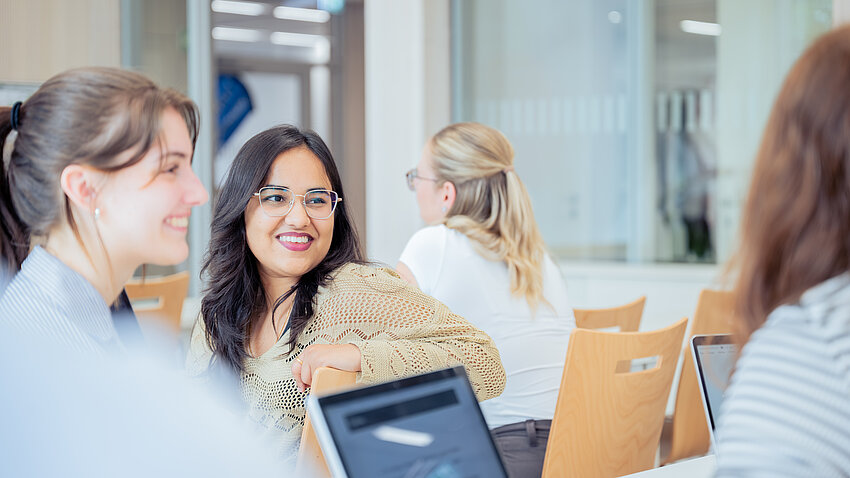 Eine Gruppe Studentinnen unterhält sich in einem hellen Vorlesungsraum.