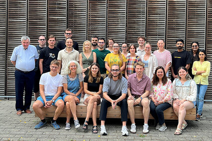 Auf dem Bild sieht man die Lehrenden und Studierenden des Masterstudiengangs Vision Science and Business (Optometry) der Hochschule Aalen zum Auftakt des Studienjahres 2026/27. Die Gruppe steht vor dem mit Holz verkleideten Studienganggebäude auf dem Campus Burren. Alle schauen fröhlich in die Kamera.