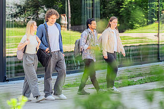 Mehrere Gruppen von Studierenden, unterhalten sich auf dem Vorplatz des Aula- / Hörsaalgebäudes.
