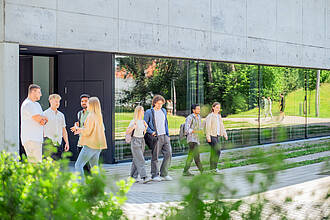 Mehrere Gruppen von Studierenden, unterhalten sich auf dem Vorplatz des Aula- / Hörsaalgebäudes.