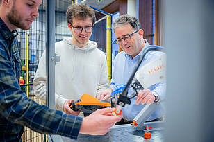 Studierende aus dem Bachelorstudiengang Mechatronik arbeiten mit einem Professor an einem Roboterarm.