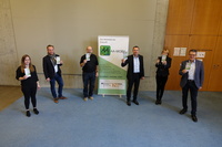 Gruppenfoto: Menschen in Anzügen posieren vor einem Plakat