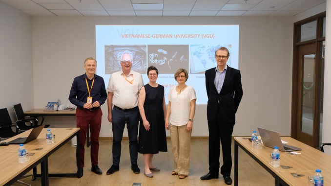Vier Personen stehen vor einer Präsentation mit dem Thema Vietnamese-German Universitiy (VGU)