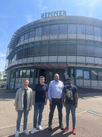 Projektteam beim gemeinsamen Projektabschluss vor Ort bei der Renner GmbH Kompressoren in Güglingen. Vier Personen im Vordergrund. Gebäude mit gebogener Fensterfront im Hintergrund. Blauer Himmel mit Sonnenschein.